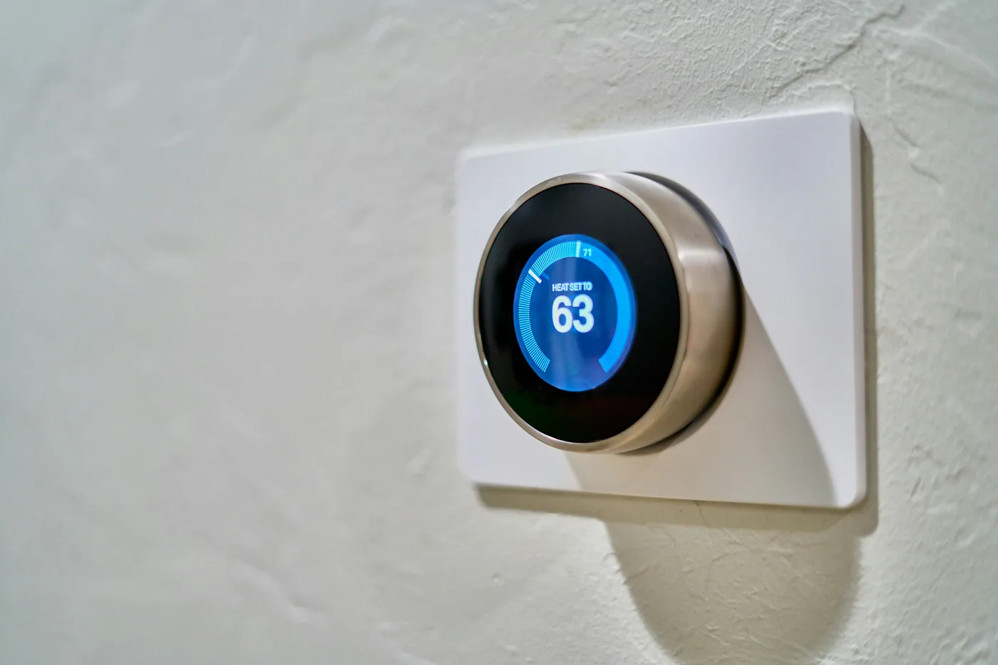 A circular digital thermostat mounted on a wall and displaying a temperature of 63°F