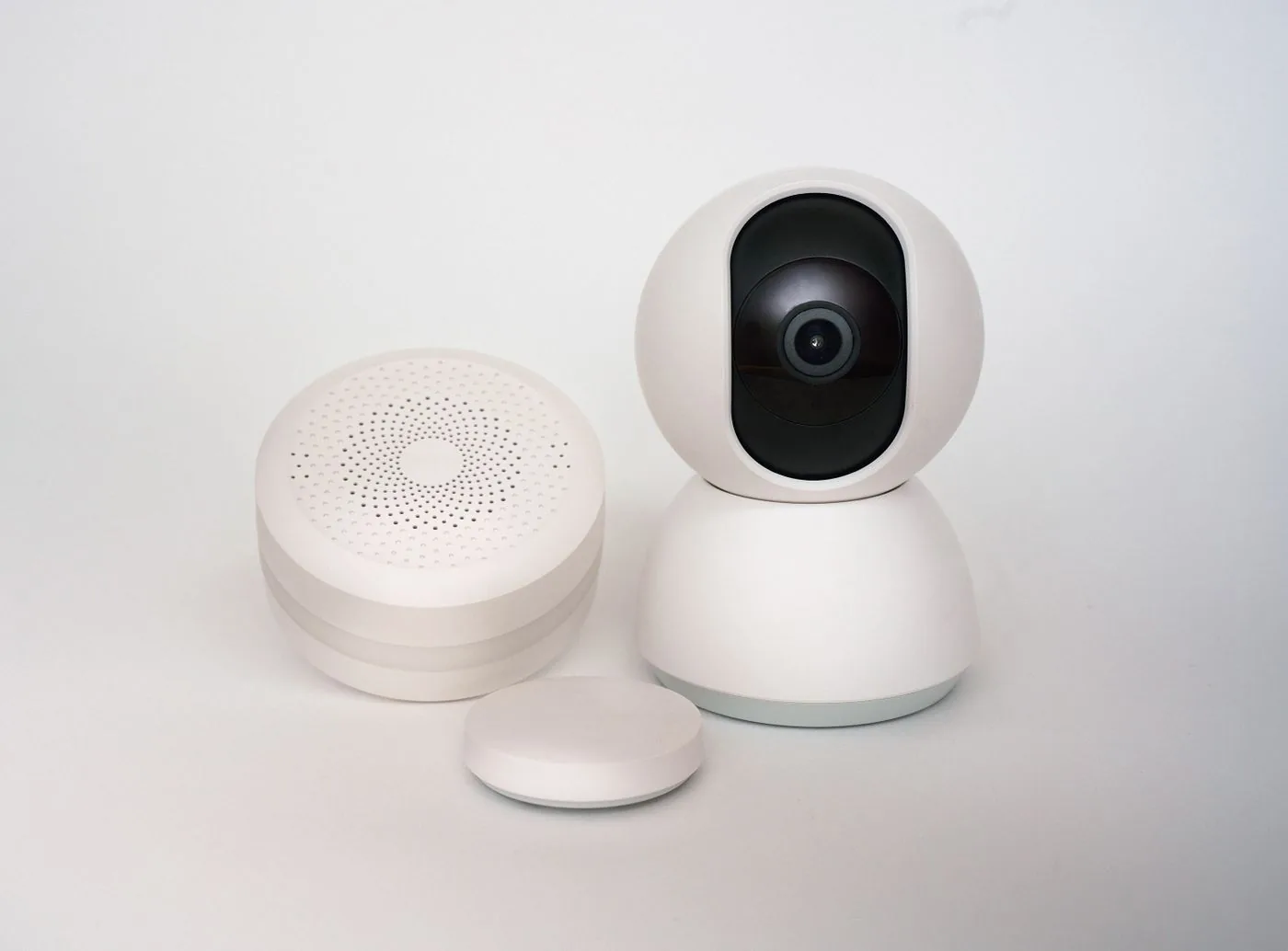 White indoor security camera with two companion smart-home sensors on a light background